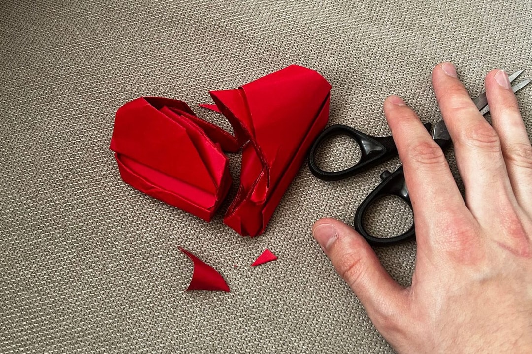 Un corazón de papel rojo cortado en pedazos junto a unas tijeras