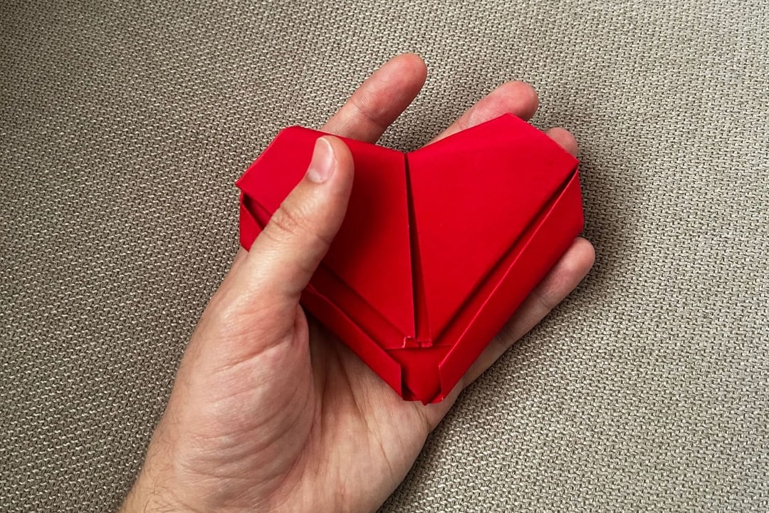 Un corazón de papel rojo sostenido con cuidado en la palma de una mano